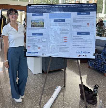 Woman stands next to research poster board and smiles